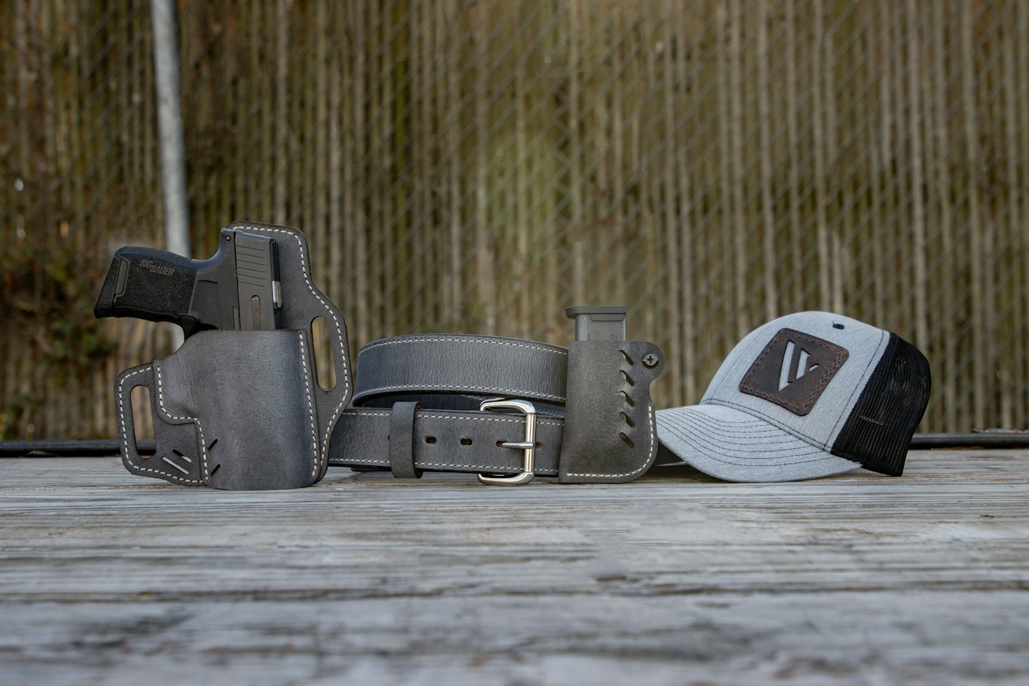 Tactical pistol, holster, belt, and cap on wooden planks.